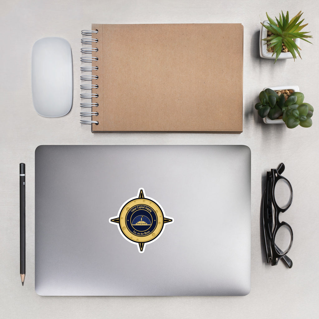 4 inch Lunar Capitol Dome Crest Sticker on a silver laptop lid beside a kraft notebook, mouse and glasses